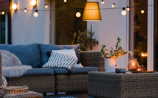 Terrasse cosy ambiance fin de journée, canapé en résine tressée et guirlande de lumière