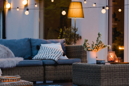 Terrasse cosy ambiance fin de journée, canapé en résine tressée et guirlande de lumière